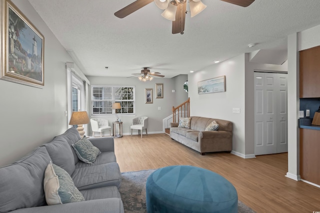 living area with ceiling fan, a textured ceiling, wood finished floors, stairs, and baseboards