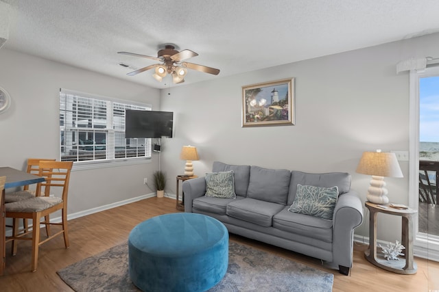 living area with a ceiling fan, wood finished floors, a textured ceiling, and baseboards