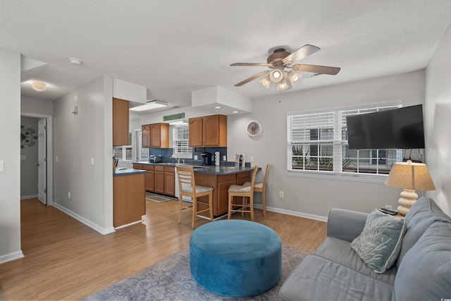 living room with ceiling fan, baseboards, light wood-style floors, and a textured ceiling