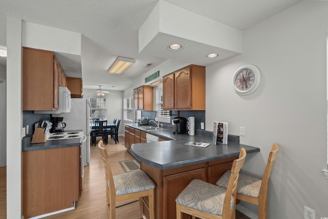 kitchen featuring a sink, dark countertops, light wood-style floors, brown cabinets, and recessed lighting