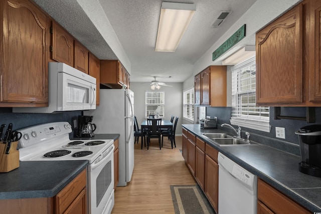 kitchen with white appliances, a sink, a ceiling fan, light wood-style flooring, and dark countertops