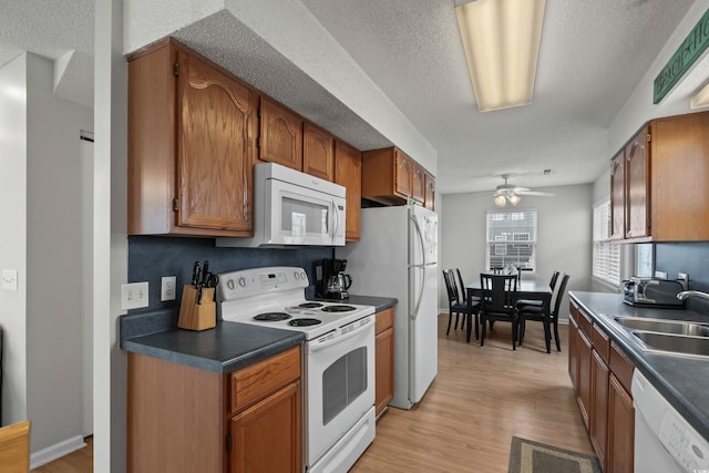 kitchen with white appliances, dark countertops, a sink, light wood-type flooring, and a ceiling fan