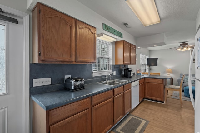 kitchen featuring a sink, dishwasher, light wood-style floors, a peninsula, and dark countertops