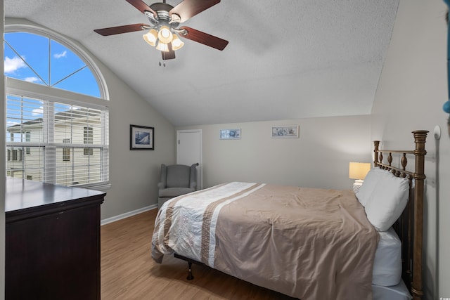 bedroom with vaulted ceiling, wood finished floors, a textured ceiling, baseboards, and a ceiling fan