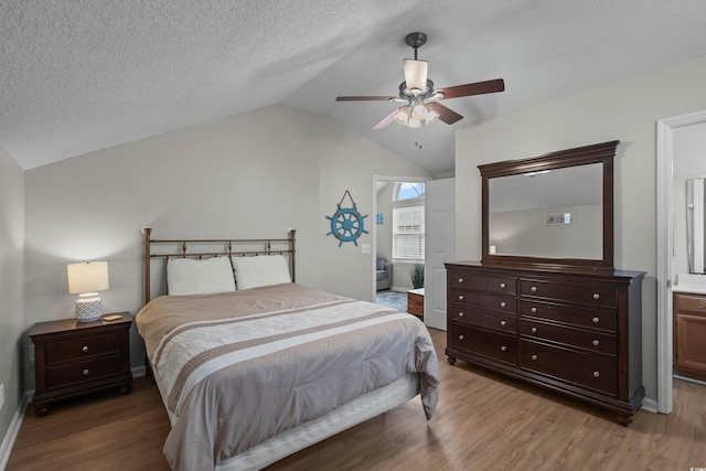 bedroom with vaulted ceiling, wood finished floors, ensuite bathroom, ceiling fan, and a textured ceiling