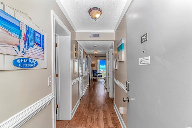 hallway featuring a textured ceiling, wood finished floors, and crown molding