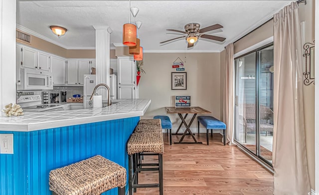 kitchen with white microwave, range, tile counters, a ceiling fan, and light wood finished floors