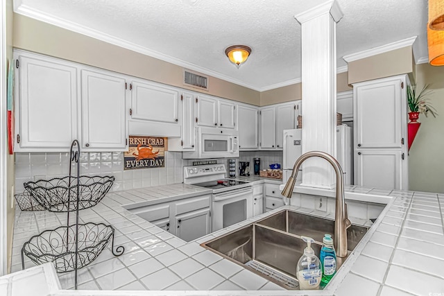 kitchen with white appliances, tile counters, a sink, decorative backsplash, and white cabinets