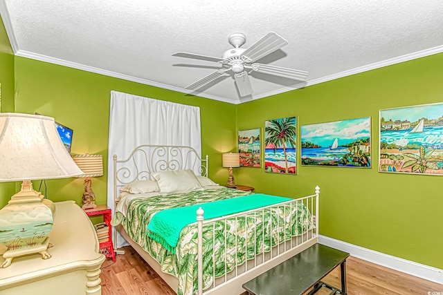 bedroom featuring wood finished floors, a textured ceiling, crown molding, a ceiling fan, and baseboards