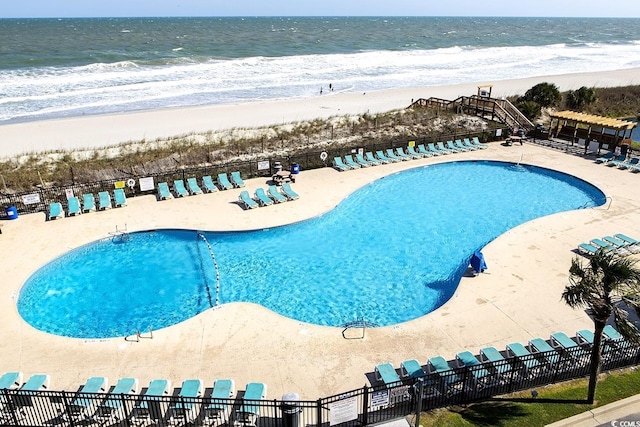 community pool with fence and view of water and beach