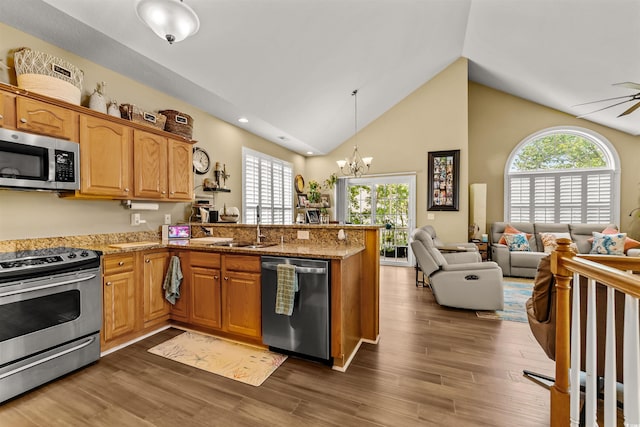 kitchen with stainless steel appliances, a sink, open floor plan, a peninsula, and light stone countertops