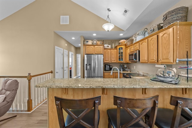 kitchen with appliances with stainless steel finishes, a peninsula, light stone counters, glass insert cabinets, and a kitchen breakfast bar