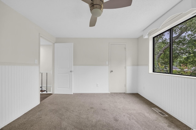 unfurnished bedroom featuring a wainscoted wall, carpet floors, and ceiling fan