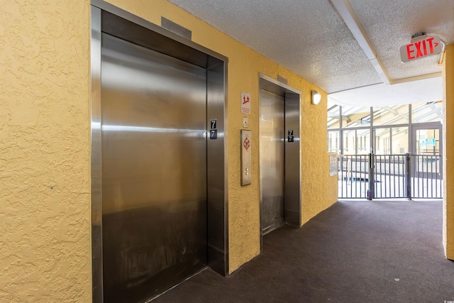 hallway featuring elevator, a textured wall, dark colored carpet, and a textured ceiling