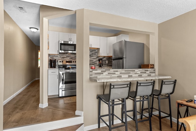 625 N Waccamaw Dr Unit 107, Murrells Inlet, SC 29576 - kitchen with appliances with stainless steel finishes, tasteful backsplash, dark wood-style flooring, white cabinets, and a breakfast bar