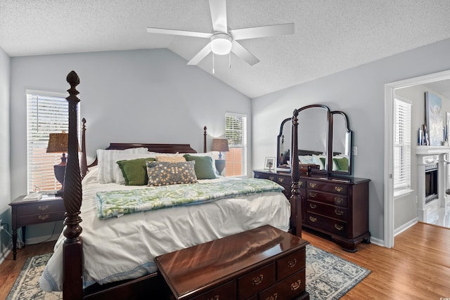 bedroom featuring wood finished floors, a textured ceiling, lofted ceiling, a glass covered fireplace, and a ceiling fan