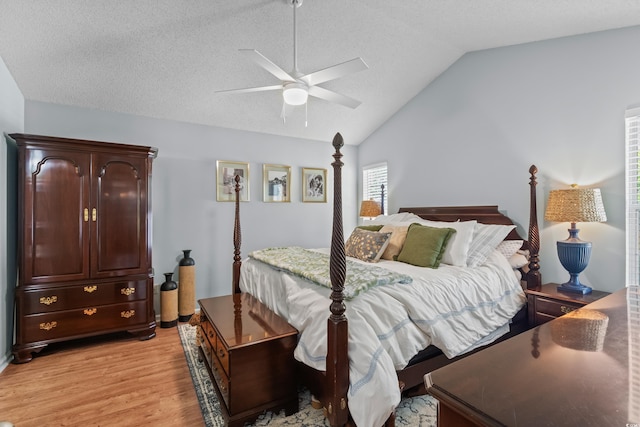 bedroom with light wood-type flooring, vaulted ceiling, ceiling fan, and a textured ceiling