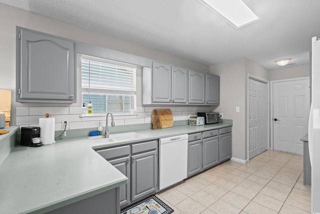 kitchen with dishwasher, gray cabinets, a sink, light countertops, and tasteful backsplash