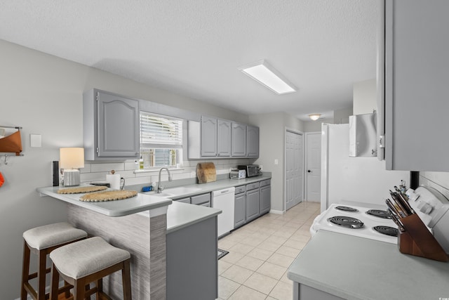 kitchen with a sink, gray cabinets, white appliances, a peninsula, and a breakfast bar
