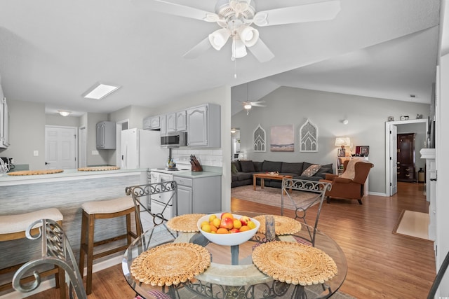 dining space featuring ceiling fan, light wood-style flooring, and vaulted ceiling