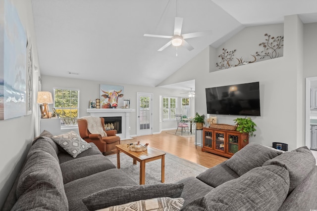 living area with ceiling fan, wood finished floors, high vaulted ceiling, and a fireplace with flush hearth