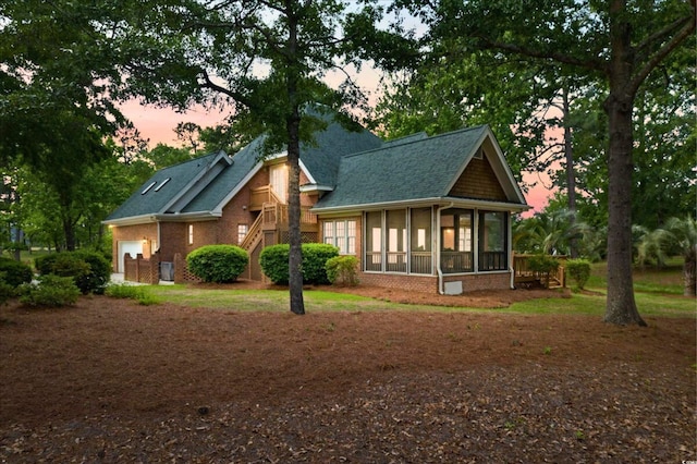 79 Windsor Cir SW, Ocean Isle Beach, NC 28469 - back of house at dusk featuring a sunroom, a garage, brick siding, and roof with shingles