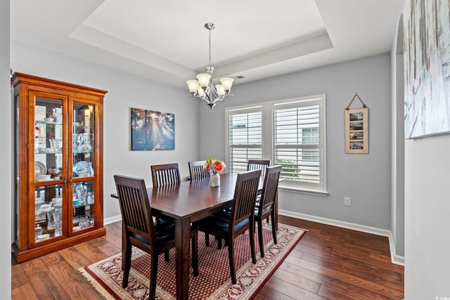 dining space featuring a chandelier, a tray ceiling, dark wood-style flooring, and baseboards