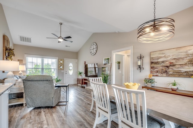 dining room featuring light wood finished floors, ceiling fan, high vaulted ceiling, and a chandelier