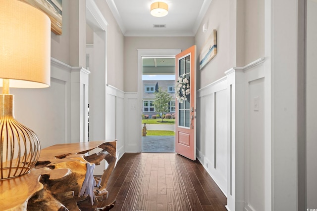 doorway with a decorative wall, dark wood finished floors, wainscoting, and crown molding