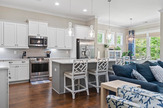kitchen featuring stainless steel appliances, open floor plan, a breakfast bar, tasteful backsplash, and white cabinetry