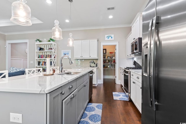 kitchen featuring appliances with stainless steel finishes, a sink, dark wood-style floors, an island with sink, and decorative light fixtures