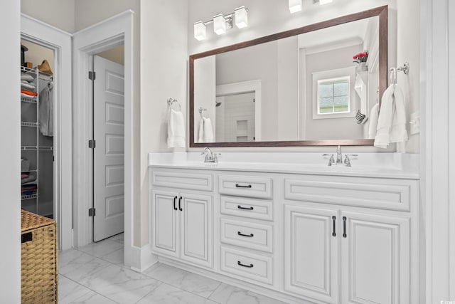 bathroom with marble finish flooring, double vanity, and a walk in closet