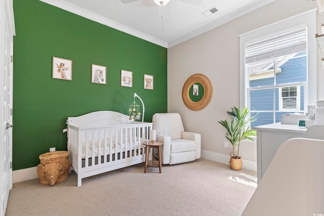carpeted bedroom featuring a crib, ornamental molding, baseboards, and ceiling fan
