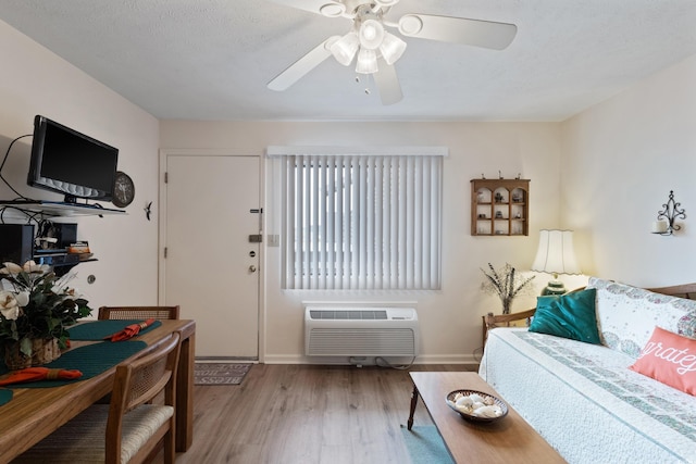 living room with a wall unit AC, wood finished floors, ceiling fan, and baseboards