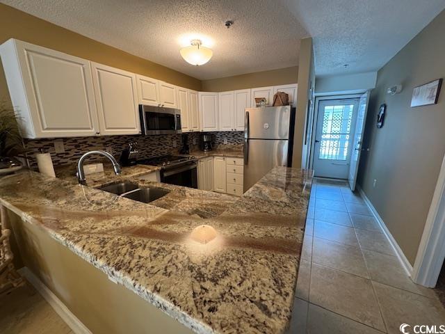 kitchen with stainless steel appliances, a sink, light stone counters, backsplash, and a peninsula