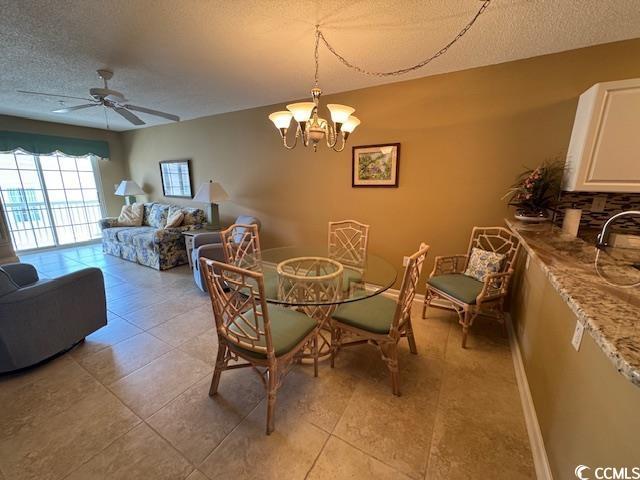 dining area featuring a textured ceiling, a ceiling fan, a chandelier, light tile patterned flooring, and baseboards