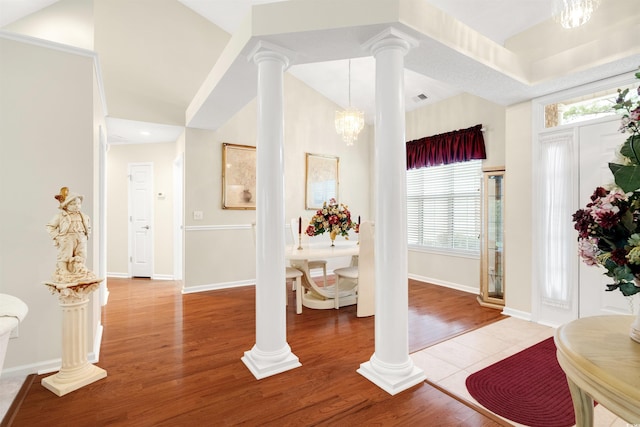 entrance foyer with decorative columns, a chandelier, wood finished floors, and baseboards