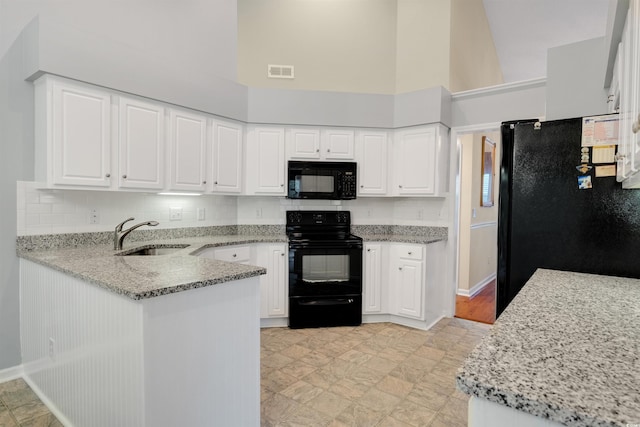 kitchen featuring black appliances, a sink, light stone counters, a towering ceiling, and white cabinetry