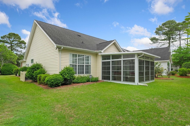 rear view of house with a sunroom, a yard, and a shingled roof