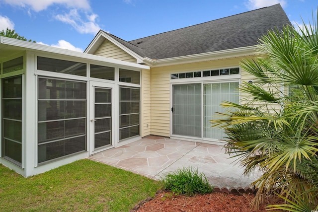 back of property featuring a sunroom, roof with shingles, and a patio area