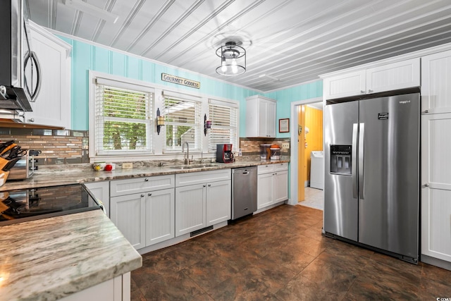 kitchen with appliances with stainless steel finishes, a sink, washer / dryer, decorative backsplash, and white cabinets