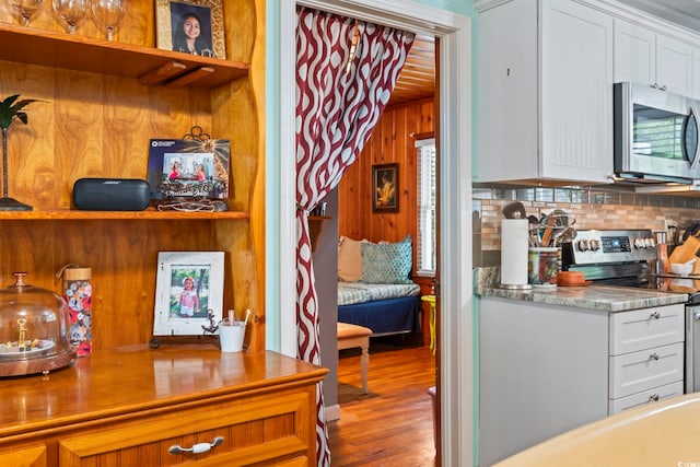 kitchen featuring appliances with stainless steel finishes, backsplash, white cabinets, wood finished floors, and wood walls