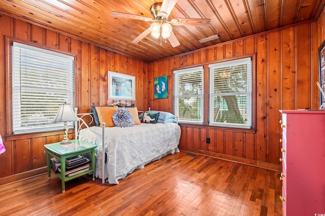 bedroom featuring wooden walls, wooden ceiling, wood-type flooring, and baseboards