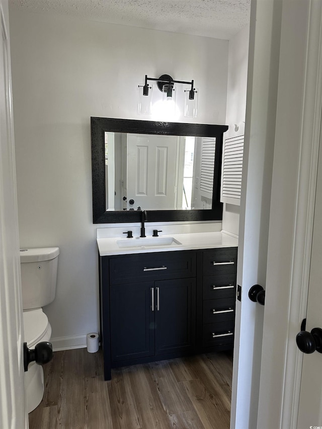 bathroom featuring wood finished floors, baseboards, a textured ceiling, vanity, and toilet