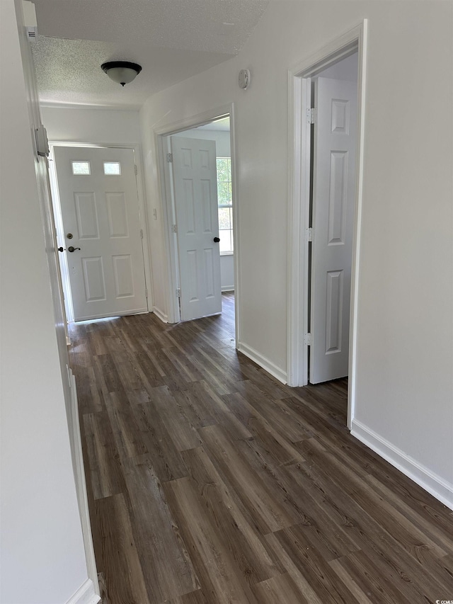 corridor featuring dark wood finished floors, baseboards, and a textured ceiling