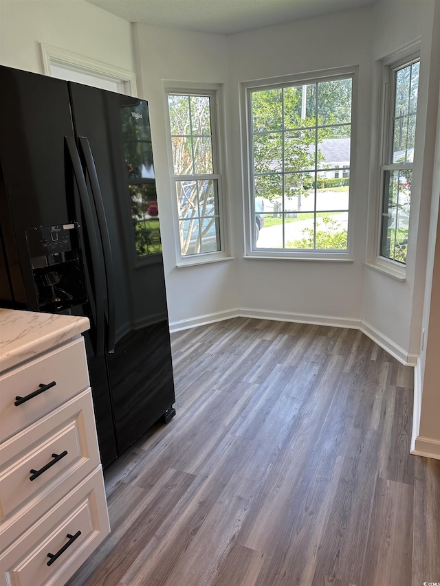 kitchen featuring black fridge with ice dispenser, wood finished floors, white cabinets, and baseboards