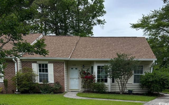 view of front of home with roof with shingles, brick siding, and a front yard