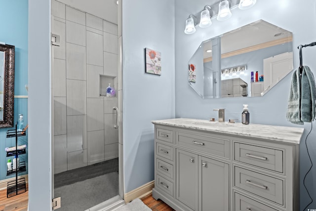 bathroom with tiled shower, vanity, wood finished floors, and baseboards