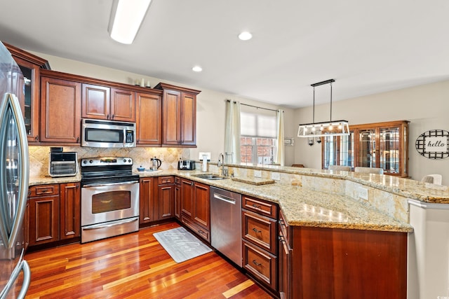 kitchen with appliances with stainless steel finishes, a peninsula, light wood-style flooring, a sink, and backsplash