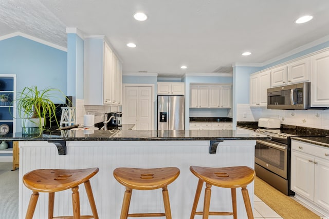 kitchen featuring stainless steel appliances, ornamental molding, a peninsula, tasteful backsplash, and dark stone countertops